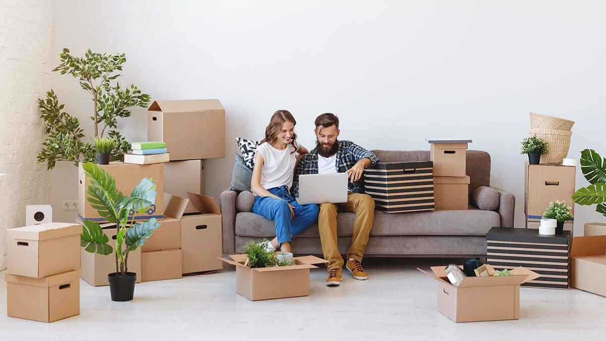 couple sitting on couch with home moving boxes, selling their home online with an iBuyer