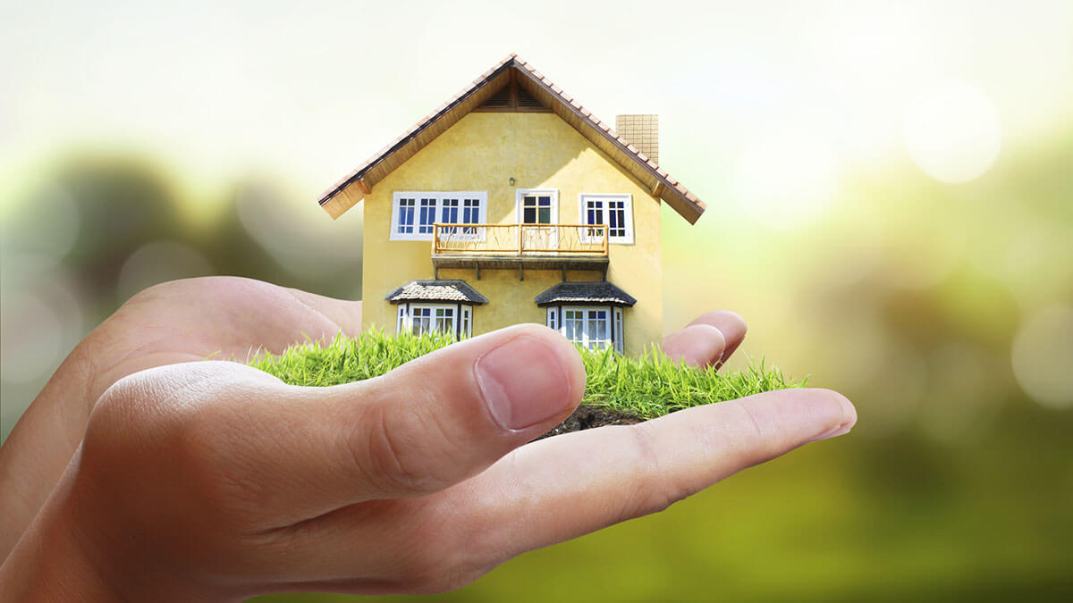 miniature house held in hands with green grass to represent spring