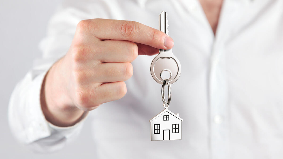 man holding house key with small home hanging on keychain