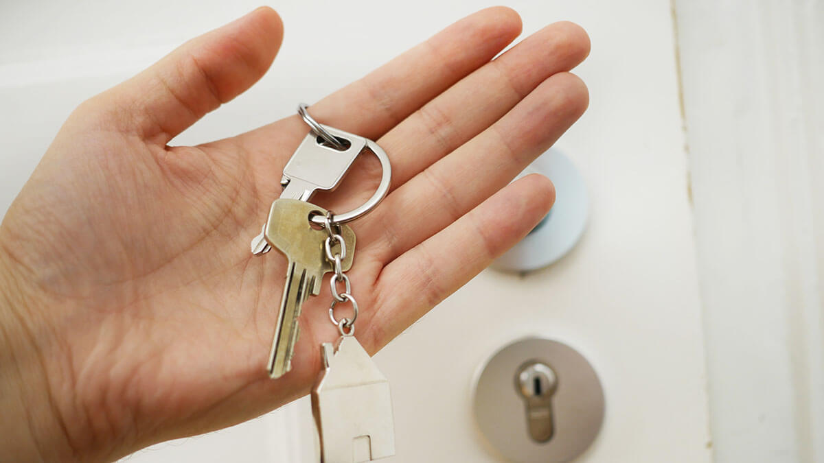 home seller holding keys of his house in palm with key lock in background