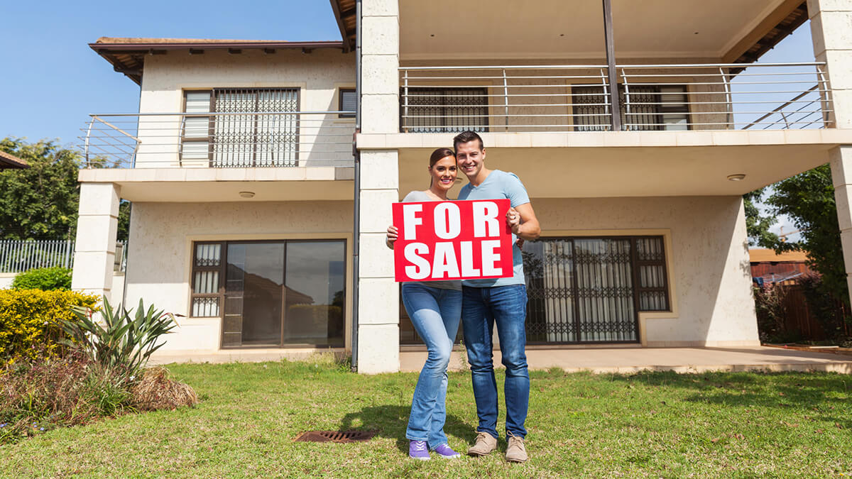 couple holding a for sale sign in front of their house