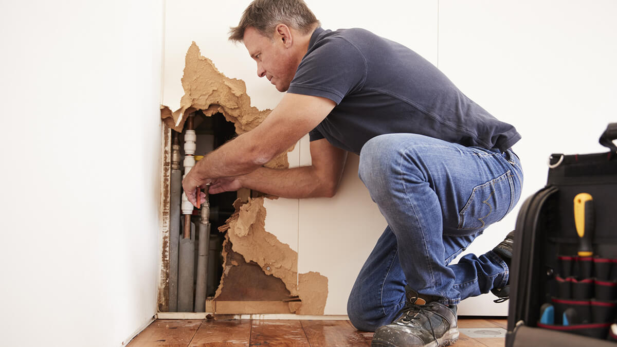 crouched person repairing water leak that caused water damage to a house